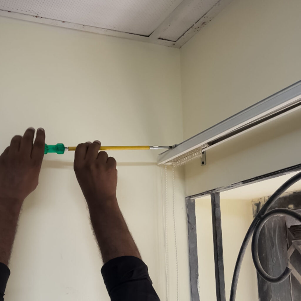 Technician adjusting vertical blinds rod during installation at Goa State Co-operative Bank branch.